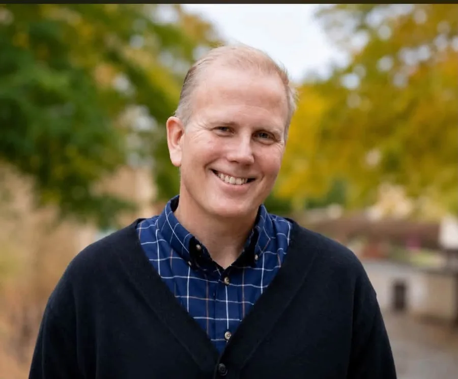 Jamie Parsley smiling outdoors in autumn, wearing a dark cardigan over a blue checked shirt