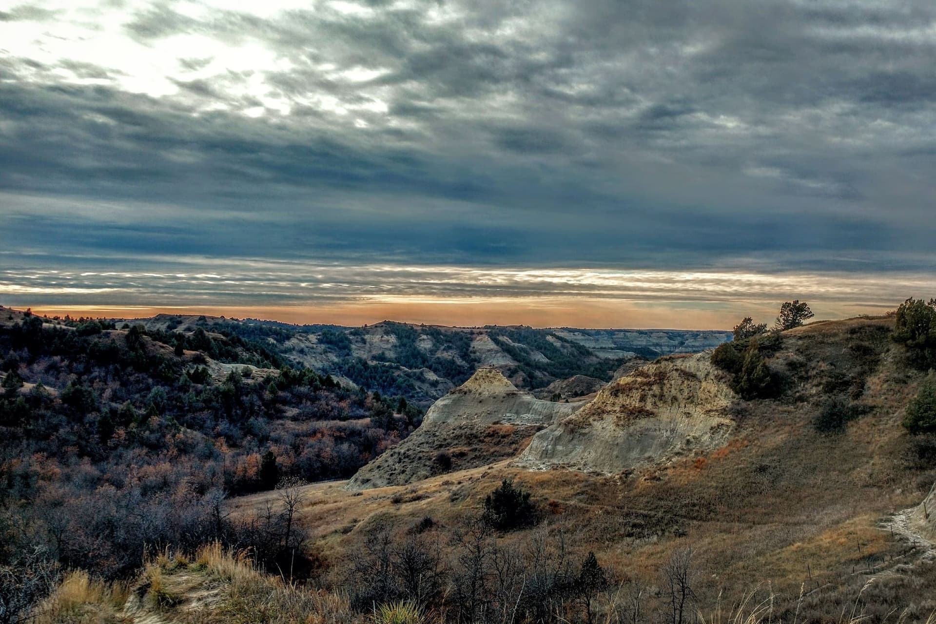 Rugged buttes and wooded ravines under a dramatic grey sky at dusk
