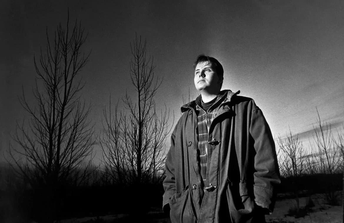 Black and white photograph of a young Jamie Parsley in a heavy coat, looking into the distance among bare trees under a wide sky